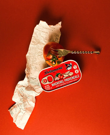Mackerel Provençale can with a fork and tomatoes on a red background